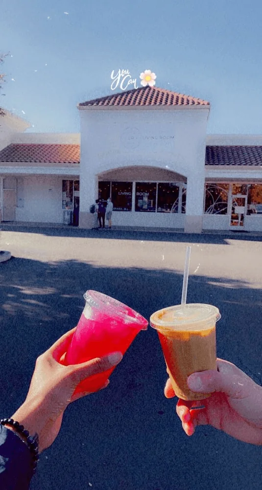 Two iced drinks held up in front of the cafe